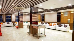 A modern hotel lobby with white sofas, colorful cushions, a central service cart, and a polished marble floor. - The Panash Hotel & Banquets (Kolkata)