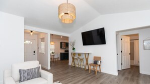 Ein modernes Wohnzimmer mit einem weißen Sofa, einem Essbereich mit Tisch und Stühlen sowie einer Küche im Hintergrund.
