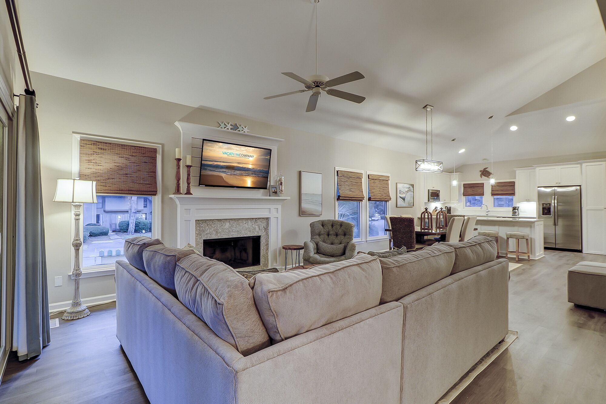 A spacious living room with a large sectional sofa, a fireplace, a television mounted above it, and a ceiling fan.