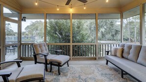 Ein Wintergarten mit Deckenventilator, großen Fenstern, einer Couch, Sesseln und einem gemusterten Teppich.