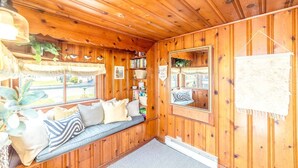 L’intérieur d’un chalet accueillant, avec un plafond en bois, un banc agrémenté de coussins, une bibliothèque et un grand miroir.