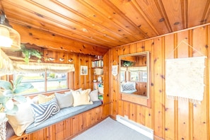 A cozy cabin interior with a wooden ceiling, a bench with cushions, a bookshelf, and a large mirror. - Wild Blue Cottage, Steps from the Beach (Cape Charles)