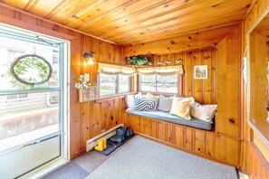 A cozy cabin interior with a wooden interior, a bench with cushions, a window with a wreath, and a door. - Wild Blue Cottage, Steps from the Beach (Cape Charles)