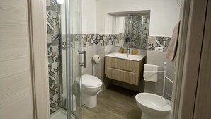 Un bagno moderno con box doccia in vetro, un water, un bidet e un lavandino con uno specchio sopra.