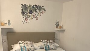 Una camera da letto con un letto, cuscini, una coperta trapuntata blu e una coperta in grigio, oltre a elementi decorativi alle pareti.