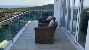 Un balcone con un divano in vimini e ringhiera in vetro che si affaccia su un panorama suggestivo.