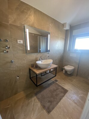 Un baño moderno con un lavamanos grande, un espejo y un inodoro.