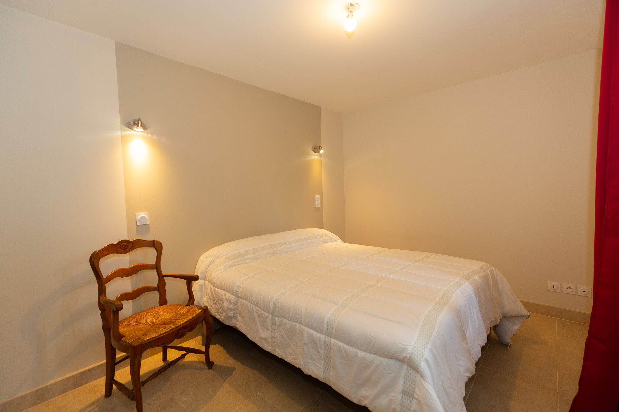 A bedroom with a single bed, a wooden chair, and two wall-mounted lights.