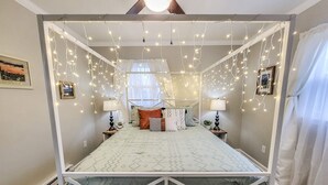 Een hemelbed met een baldakijn, lichtjes en uitzicht op het omliggende landschap door een raam.