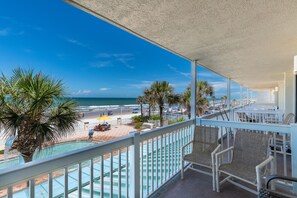 Uma varanda com vista para a praia e o oceano, com cadeiras de vime e piscina.