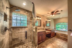 A bathroom with a glass-enclosed shower, a vanity with a sink, a mirror, and a window.