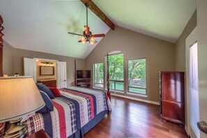 A bedroom with a bed, a ceiling fan, a television, and a large window.