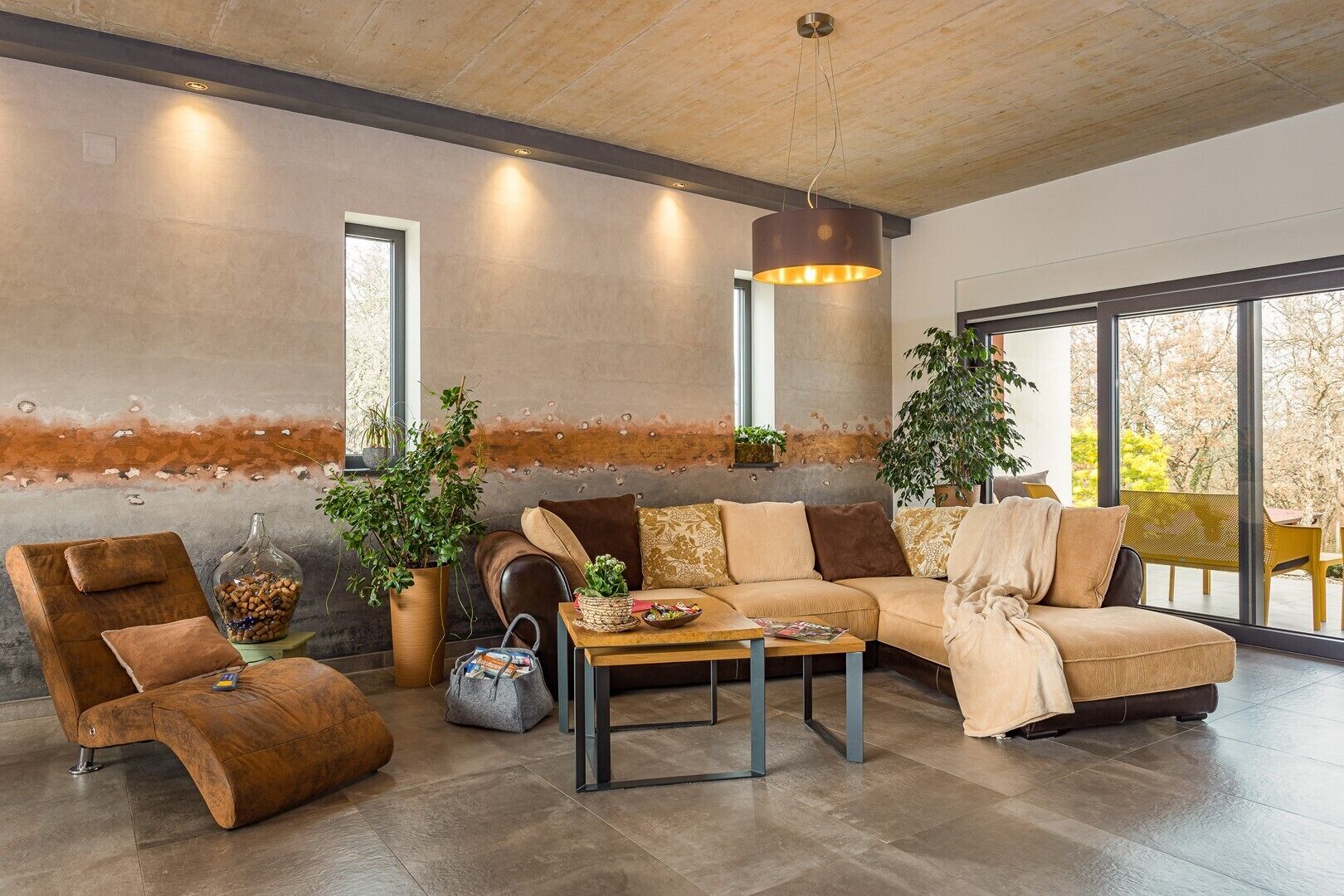 A modern living room with a sofa, armchair, and coffee table, featuring large windows and a view of the outdoors.