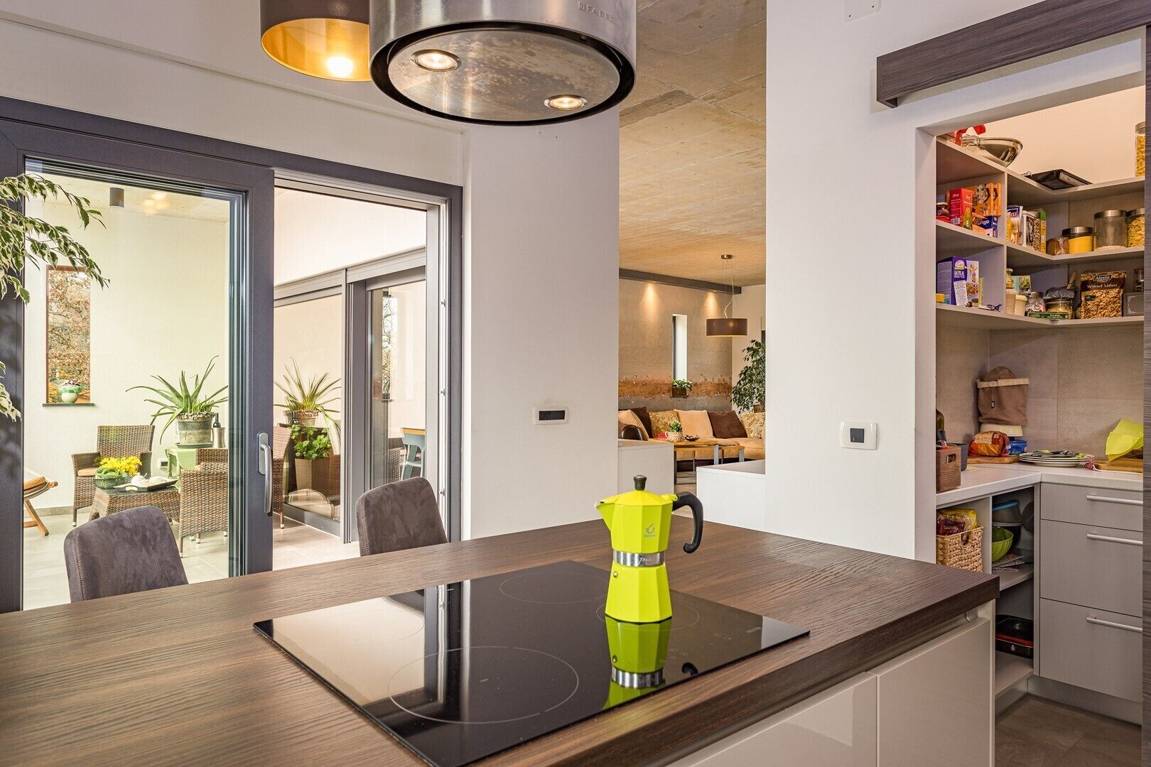 Une cuisine moderne dotée d’une plaque de cuisson à induction intégrée, d’une cafetière jaune vif et d’un garde-manger rempli de divers produits alimentaires.
