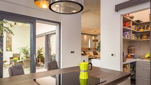 Uma cozinha moderna com uma placa de indução embutida, uma cafeteira amarelo-vivo e uma despensa repleta de diversos alimentos.