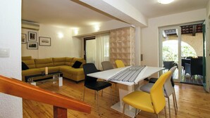 A modern living room with a wooden floor, a yellow sofa, a dining table with chairs, and a staircase.