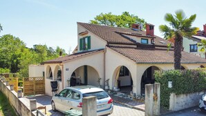 A two-story house with a tiled roof, arched doorways, and a car parked in the driveway.