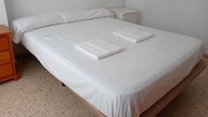 A neatly made bed with white linens and two folded towels, a wooden nightstand, and a wall socket. - Bonaire H-6º Solo Familias! (Playa de Gandía)