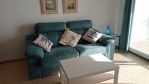A teal sofa with three patterned cushions, a white coffee table, and two framed artworks on the wall. - Bonaire H-6º Solo Familias! (Playa de Gandía)