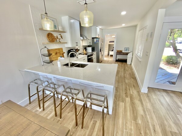 A modern kitchen with a large island, bar stools, pendant lighting, and a view of the backyard.