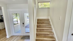 Un escalier en bois menant à l’étage supérieur, des murs blancs et une porte avec des panneaux de verre.