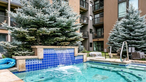 Ein mit blauen Fliesen ausgekleideter Swimmingpool, umgeben von Bäumen und einem Gebäude mit Balkonen.