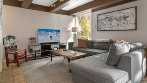 Ein Wohnzimmer mit grauem Sofa, einem Holztisch, einem Fernseher und einem Gemälde an der Wand.