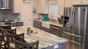 A modern kitchen with a central island, stainless steel appliances, and pendant lighting. - Tequila Sunrise 4 Bedroom Home by RedAwning (Navarre)