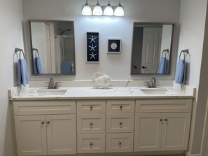 A bathroom with two sinks, a large mirror, and a fish decoration. There are towels hanging on hooks and a small framed picture on the wall. - Coastal Retreat 3 Bedroom Home by RedAwning (Navarre)