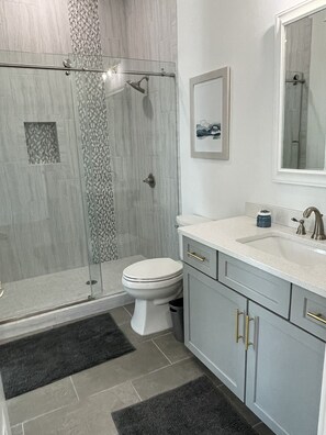 A modern bathroom with a glass-enclosed shower, a white toilet, and a sink with a mirror above it.