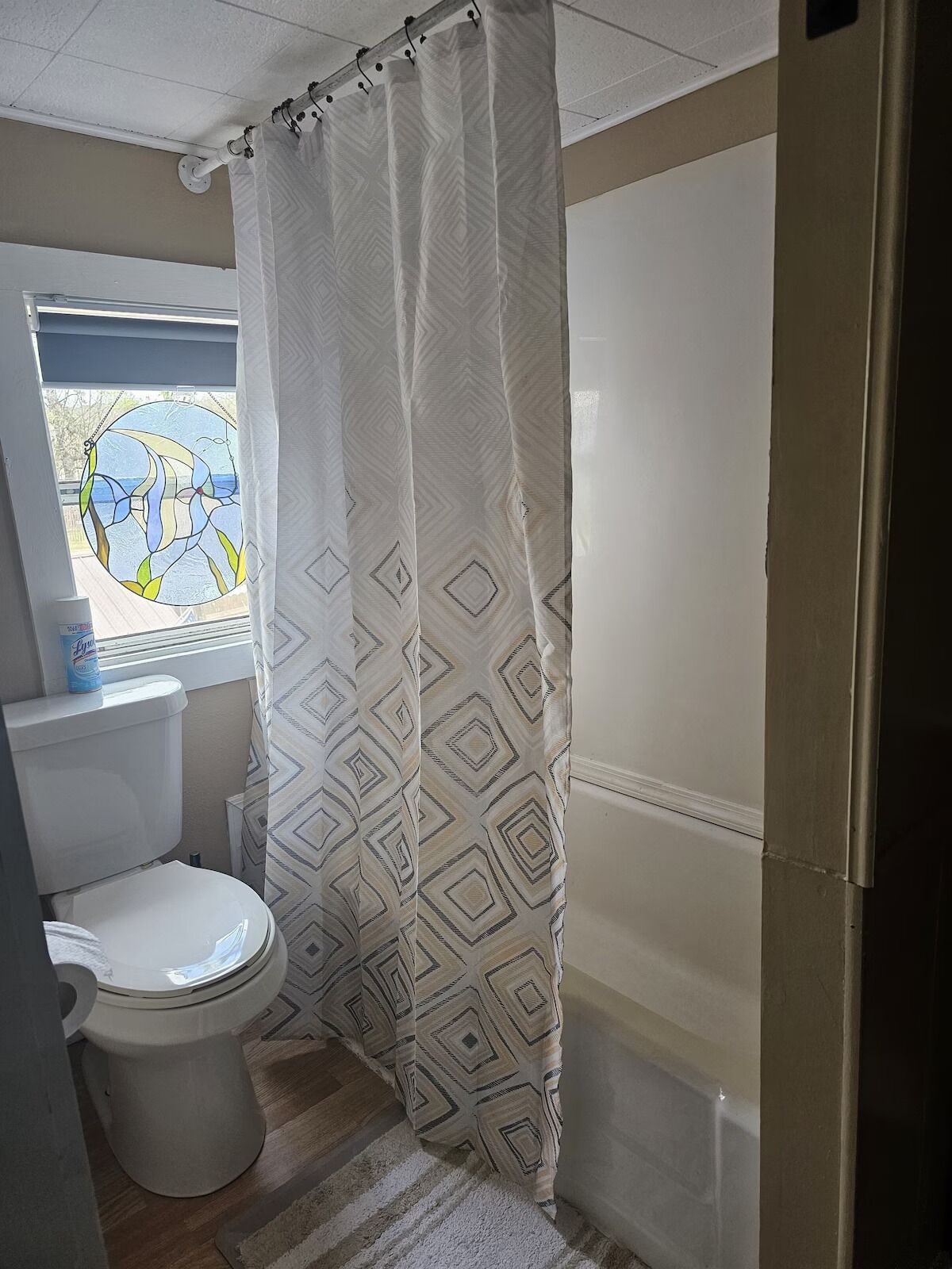 A bathroom with a toilet, a window with a stained glass design, and a shower curtain with a geometric pattern.