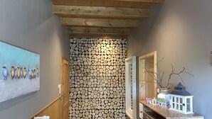 A hallway with a wooden ceiling, a wall covered with logs, a painting of birds, and a cabinet with a lantern.