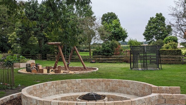 A circular stone fire pit with a metal cover, surrounded by a stone border.