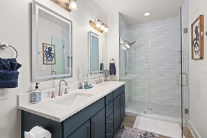 A modern bathroom with a double sink vanity, a glass shower enclosure, and a large mirror. - Pelican Place -Beach Front-Ocean View- Next to Beach Club- 3BD/2BA. Sleeps 8 (Galveston)