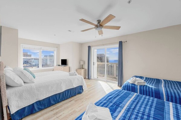 Habitación de hotel con cama, escritorio, silla, ventana, ventilador de techo y balcón con vistas.