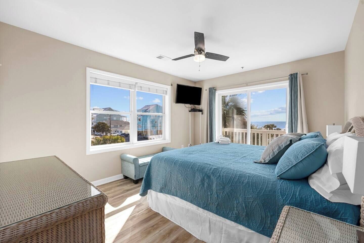 Une chambre à coucher avec un lit, un ventilateur de plafond, un téléviseur fixé au mur et de grandes fenêtres donnant sur la mer.