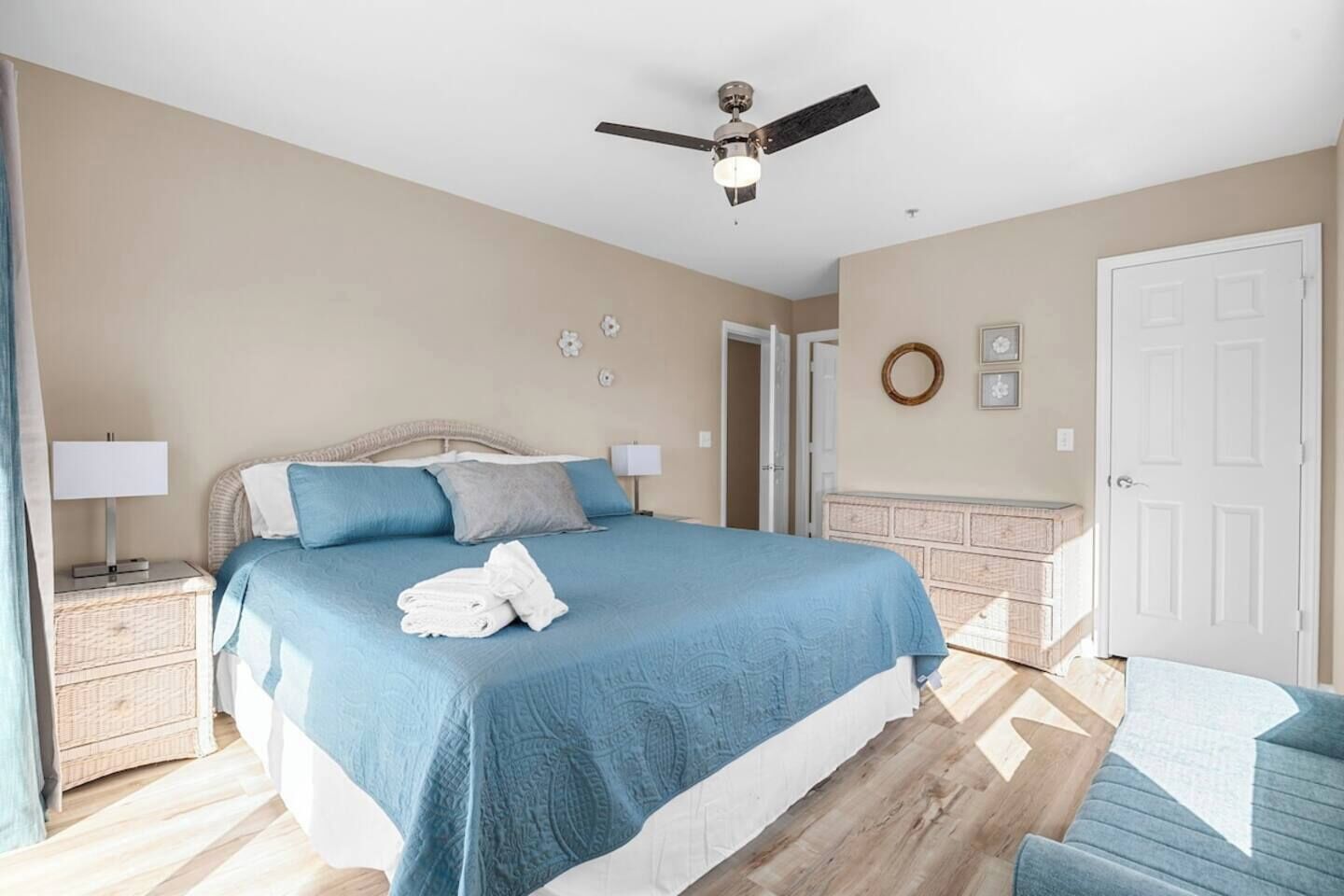 Een slaapkamer met een bed, nachtkastjes, een plafondventilator, een deur en een muur met een ronde decoratie.