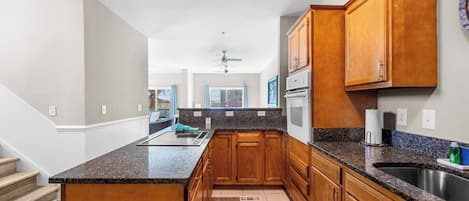 A kitchen with wooden cabinets, granite countertops, a built-in oven, and a stainless steel sink.