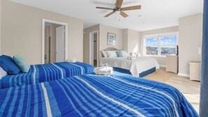 A hotel room with two beds, a ceiling fan, a large window with a view, and a door leading to another room.