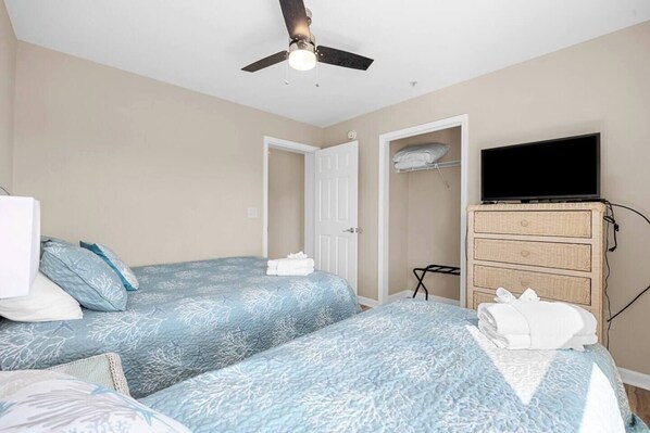 A bedroom with two beds, a ceiling fan, a television, and a dresser.