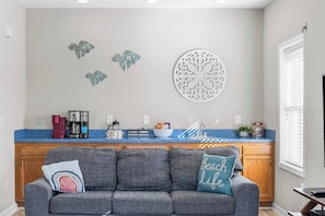 Una cocina moderna con encimera azul, un sofá gris con un cojín de temática marina y decoración en la pared.