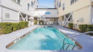 A swimming pool with a 3 ft depth marker, surrounded by buildings with balconies and a covered walkway.