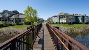 A wooden bridge over a calm water body, connecting two rows of townhouses with a clear sky above. - Condo with elevator and POND VIEWS! - 12 Pondview Lane (Lewes)