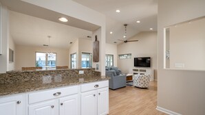 A spacious kitchen with granite countertops, white cabinetry, and a large island. There is a living area with a sofa and a television. - Condo with elevator and POND VIEWS! - 12 Pondview Lane (Lewes)