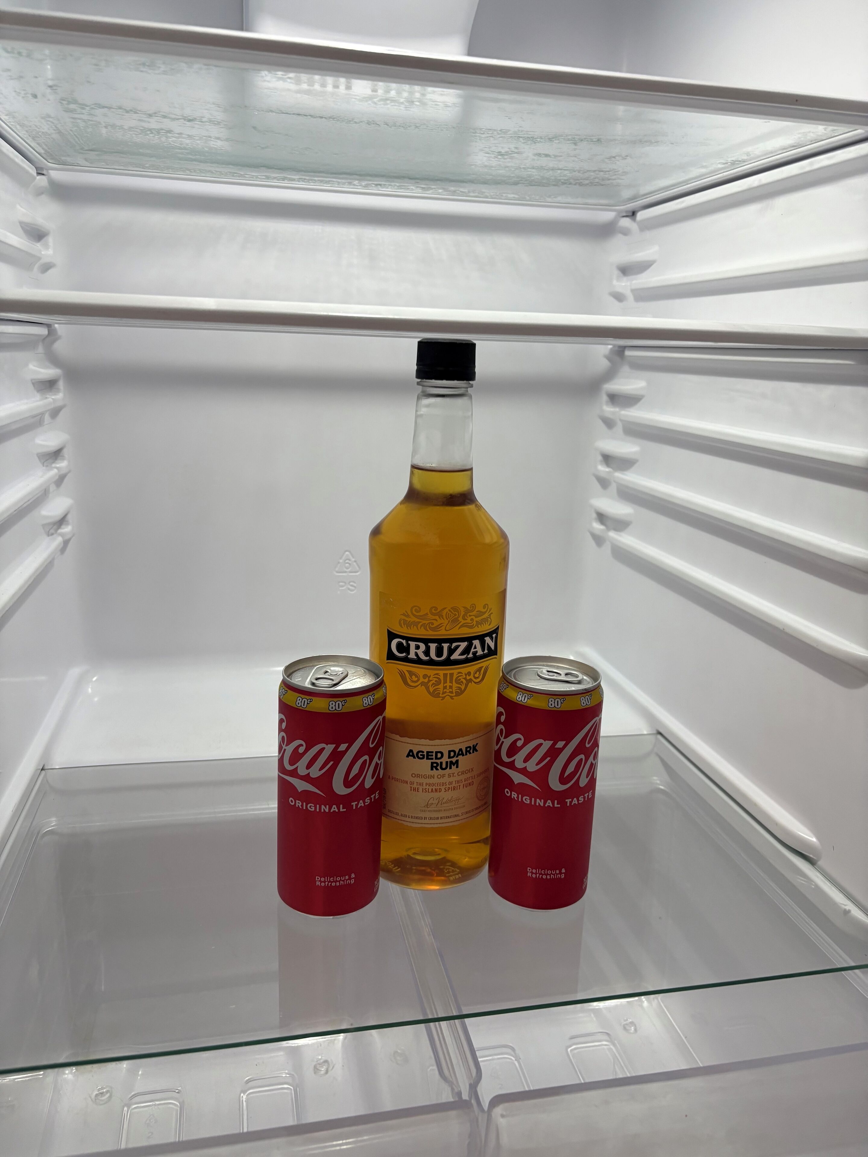 Ein leerer Kühlschrank mit einer Flasche Cruzan Aged Dark Rum und zwei Dosen Coca-Cola.