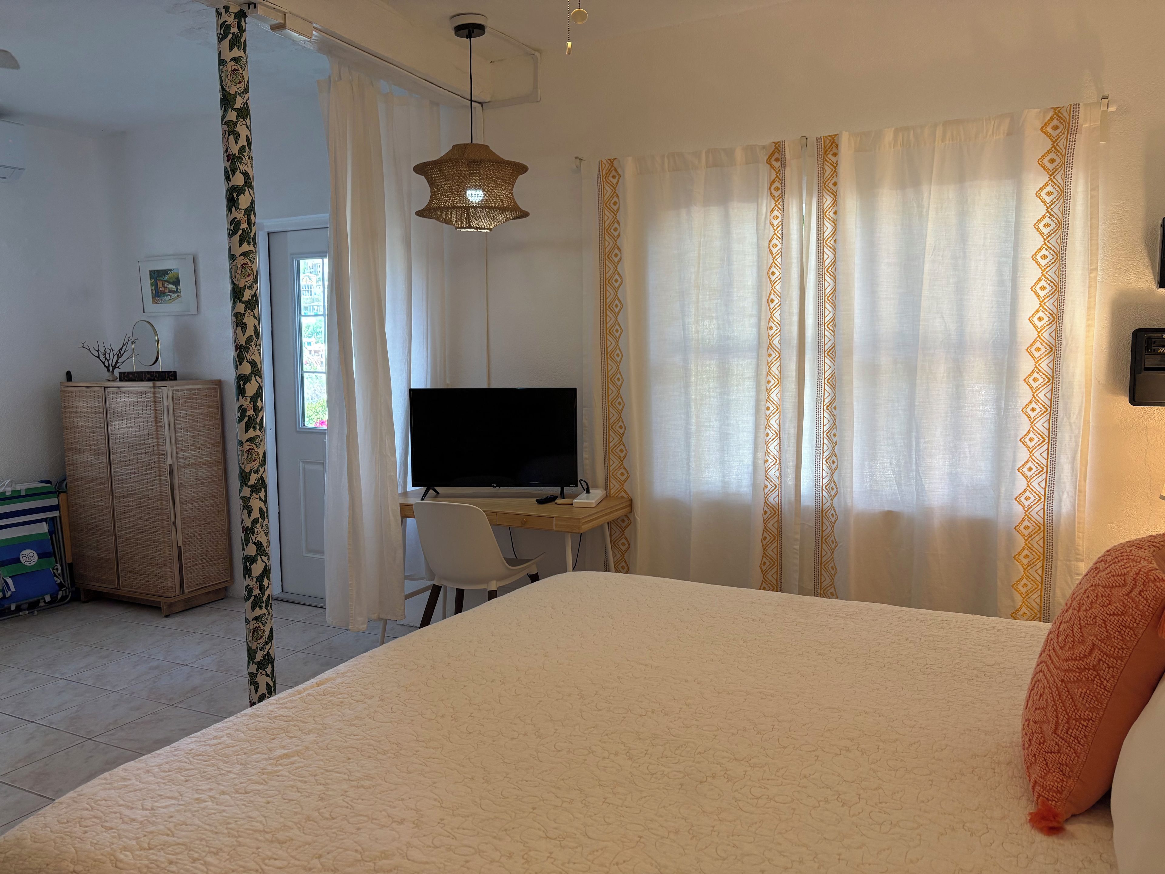 Ein Schlafzimmer mit einem Bett, einem Schreibtisch mit Fernseher, einem Kleiderschrank und Vorhängen.