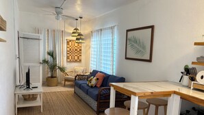 Ein gemütlicher Wohnbereich mit einer Couch, einem kleinen Esstisch, einem Fernseher und einem Deckenventilator.