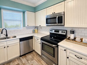 A modern kitchen with white cabinetry, stainless steel appliances, and a wooden floor.