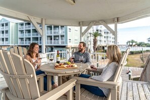 Three people seated at a round table with a food platter, enjoying drinks in an outdoor setting with a view of buildings in the background.