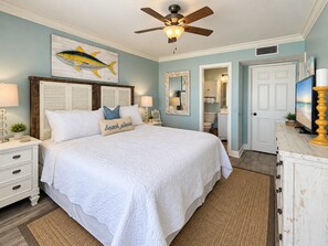 A bedroom with a bed, a ceiling fan, a fish artwork on the wall, and a bathroom visible through an open door.
